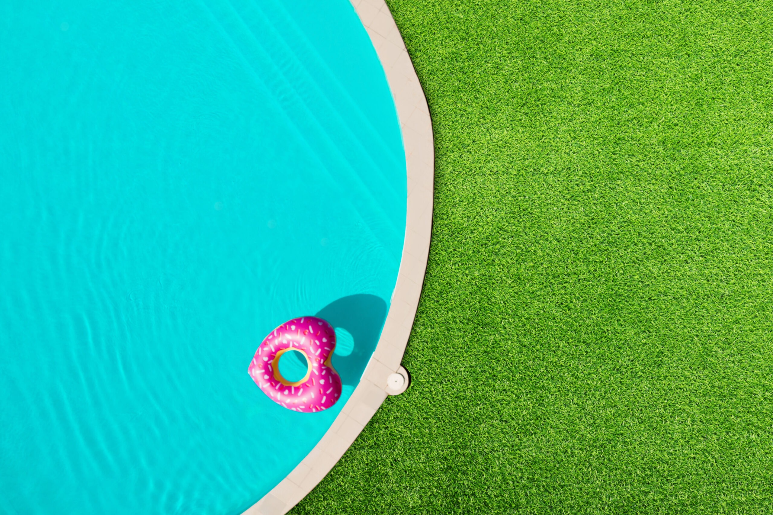 Heart-shaped pink pool float in a blue swimming pool beside realistic artificial turf grass